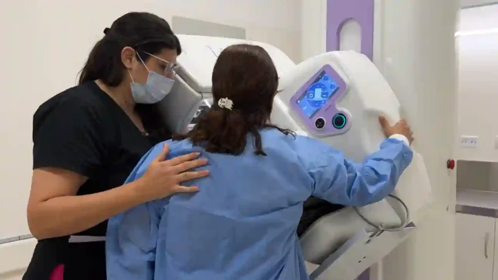 Técnica médica con mascarilla ayuda a una paciente a posicionarse frente a una máquina de mamografía